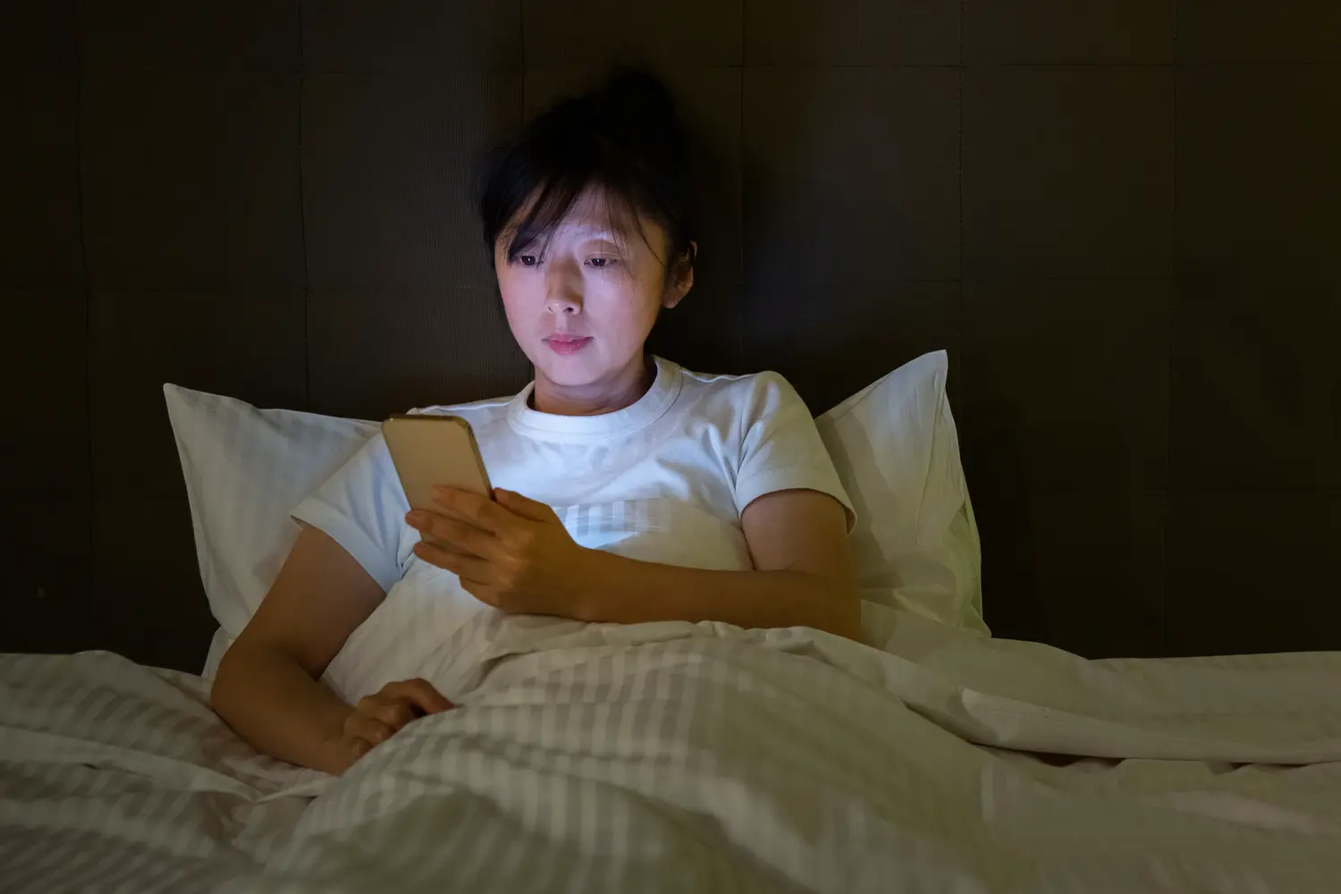 Woman lying in bed at night looking at her smartphone